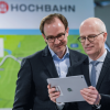 HOCHBAHN-Chef Henrik Falk (l.) und Hamburgs Erster Bürgermeister Dr. Peter Tschentscher schauen auf ein Tablet.