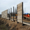 Arbeiter errichten eine Holzspundwand entlang der Baustelle.
